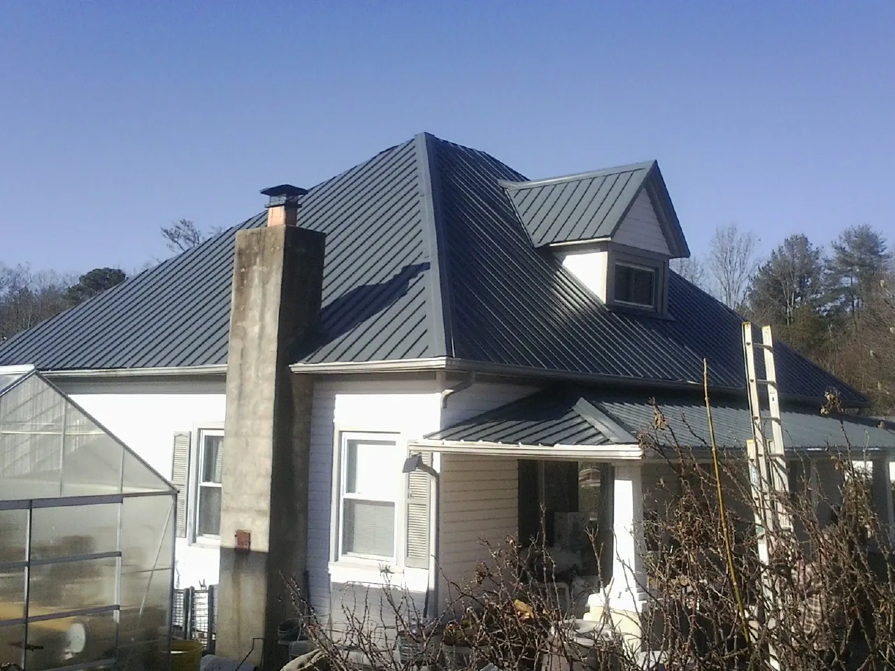 Dark blue standing seam metal roof on a white farmhouse with dormer — Slate & Tile Roof Repair by Roofing Brothers in Carter Lake