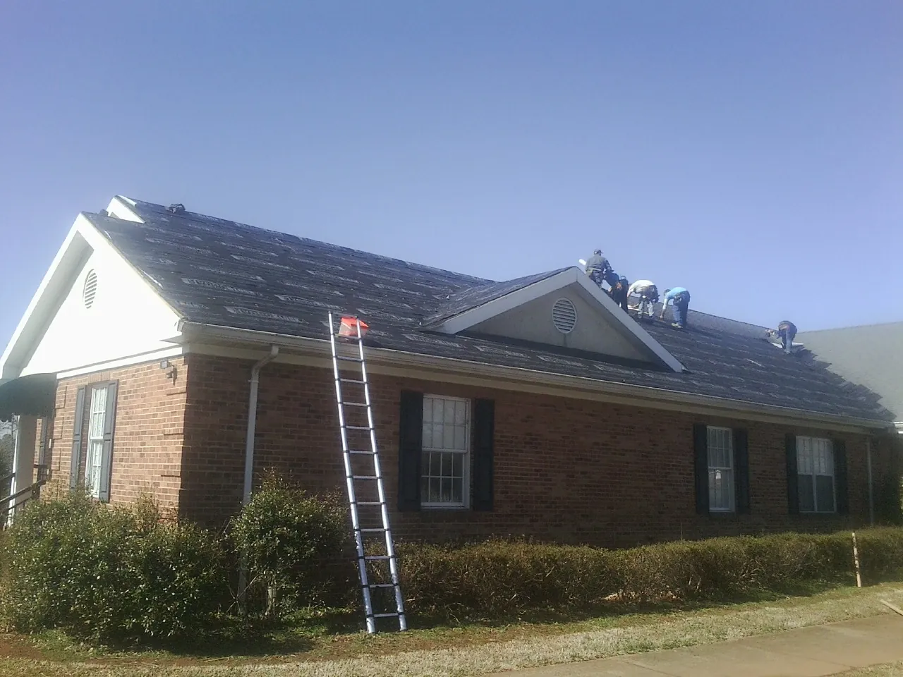 Crew tearing shingles off a brick ranch roof with a ladder set — Emergency Roof Repair work by our crew in Carter Lake