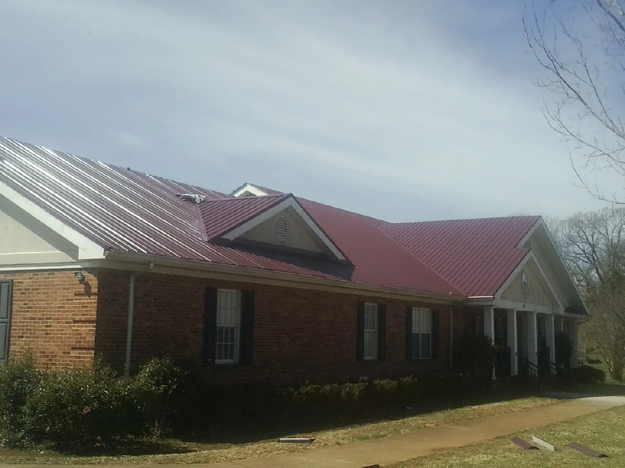 Red metal roof with gabled entries on a long brick building, from a Hail Damage Roof Repair job in Carter Lake