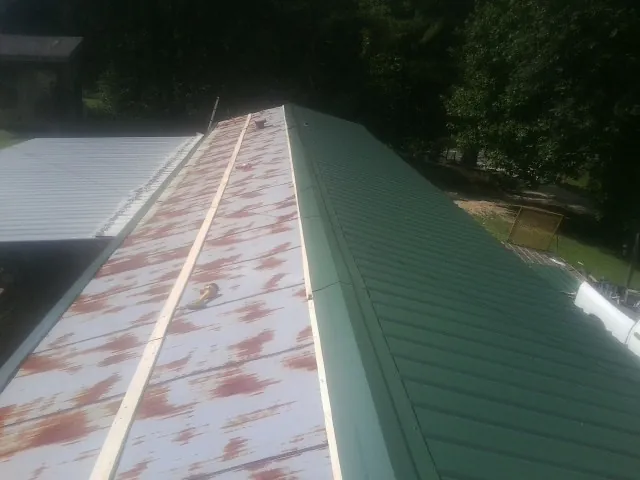 Old rusted panels beside newly installed green metal roofing — Wind Damage Roof Repair by Roofing Brothers in Carter Lake