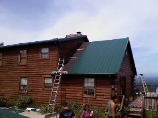 Green metal roof going on a two story log home with ladders set in Carter Lake