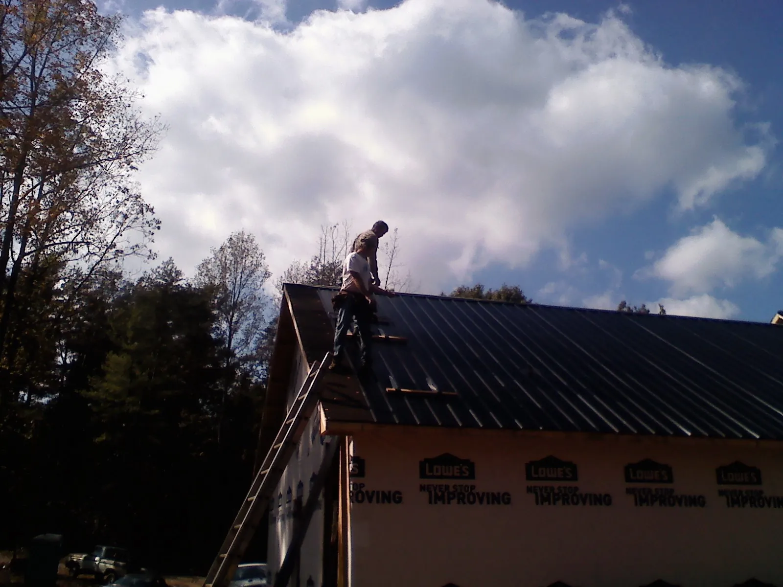 Roofer fastening dark metal panels high against a cloudy sky, from a Roof Inspection job in Carter Lake