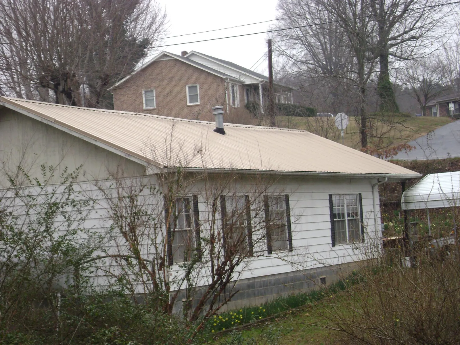 Tan metal roof on a white sided house set into a hillside — Commercial Roofing by Roofing Brothers in Carter Lake