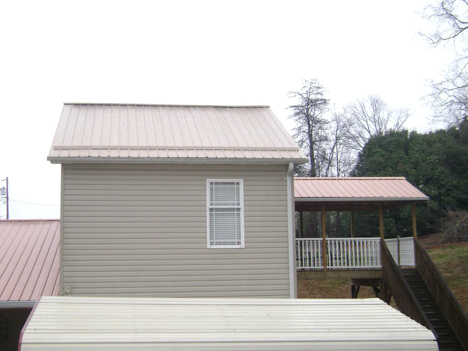 Tan metal roofs on a two story addition and attached porch, from a Roof Replacement job in Carter Lake